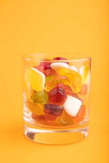 Various fruit jelly candies in drinking glass on orange pastel background. side view, close up