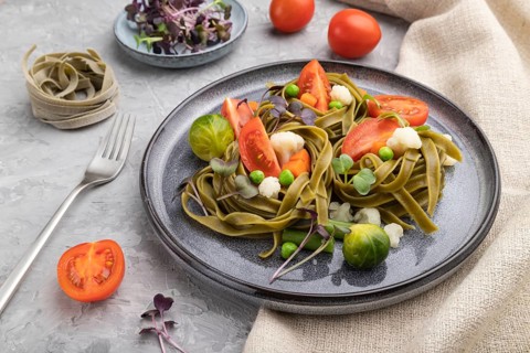 Tagliatelle green spinach pasta with tomato, pea and microgreen sprouts on a gray concrete