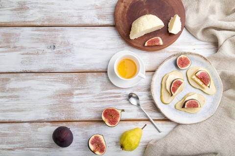 Summer appetizer with pear, cottage cheese, figs and honey on a white wooden background and linen