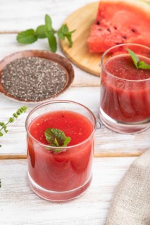 Watermelon juice with chia seeds and mint in glass on a white wooden background with linen textile.