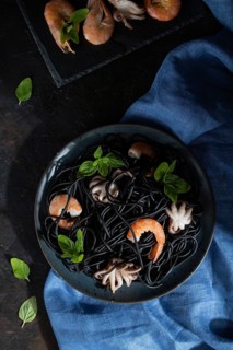 Black cuttlefish ink pasta with shrimps or prawns and small octopuses on black concrete background