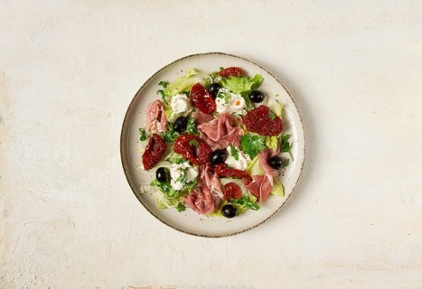 Salad with dried tomatoes, prosciutto, soft cheese, olives, homemade, top view