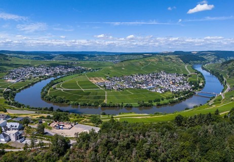 Panoramic view of a winding river surrounded by vineyards and a village with blue sky and clouds in