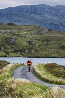 Lonely biker cycling through the Scottish Highlands on heavily laden touring bicycle along single