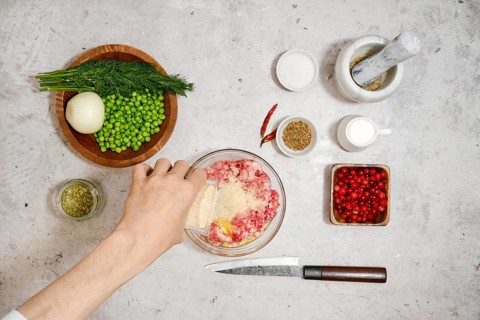 Top view of male hand pouring breadcrumbs into a bowl of minced meat. Process of preparing minced