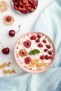 Rice flakes porridge with milk and strawberry in ceramic bowl on white concrete background and blue