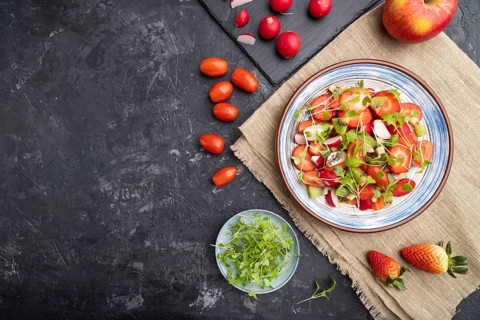 Vegetarian fruits and vegetables salad of strawberry, kiwi, tomatoes, microgreen sprouts on black