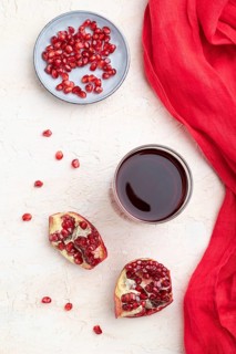 Glass of pomegranate juice on a white concrete background with red textile. Top view, close up,