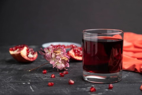 Glass of pomegranate juice on a black concrete background with red textile. Side view, close up,