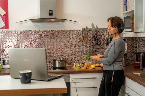 Woman, mid-50s, works from home, with laptop and communicates with colleagues via headset, home