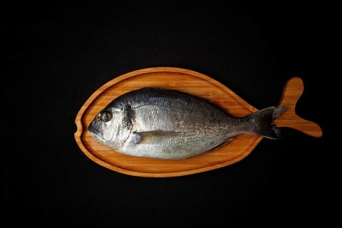 Raw fresh dorado fish, wooden plate in the shape of a fish, on a black table, top view, no people