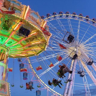 Illuminated chain carousel and Ferris wheel at night with cheerful people, funfair, wave flight,