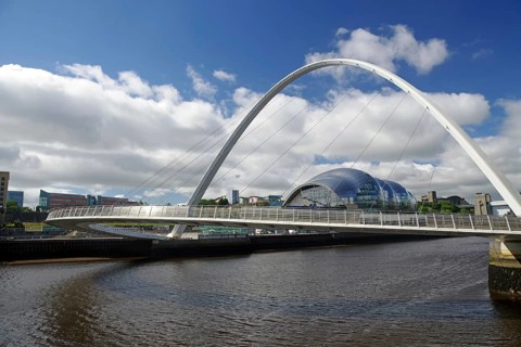 A modern bridge spans a river, behind which a futuristic glass building stands out, Milleniums