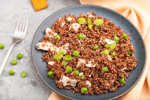 Quinoa porridge with green pea and chicken on ceramic plate on a gray concrete background and