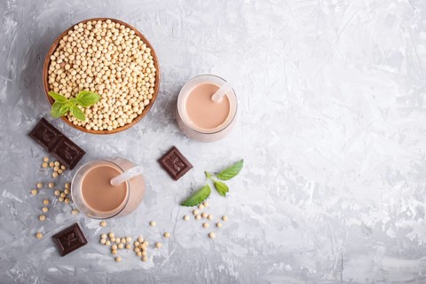 Organic non dairy soy chocolate milk in glass and wooden plate with soybeans on a gray concrete
