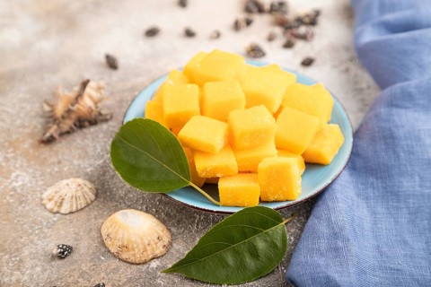 Dried and candied mango cubes on blue plate on brown concrete background and linen textile. Side