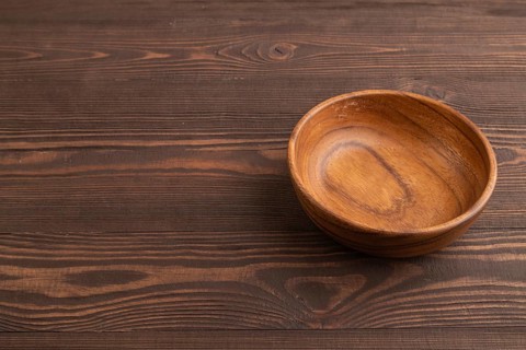 Empty brown wooden bowl on brown wooden background. Side view, copy space