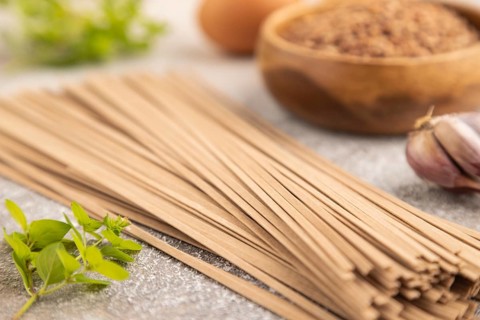 Japanese buckwheat soba noodles with tomato, eggs, spices, herbs on brown concrete background. Side