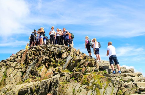 Walkers crowd onto the summit point, Mount Snowdon, Gwynedd, Snowdonia, north Wales, UK