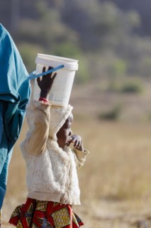 Very small girl carrying a heavy bucket of water on her head, Maraban Dare, 07/02/2024