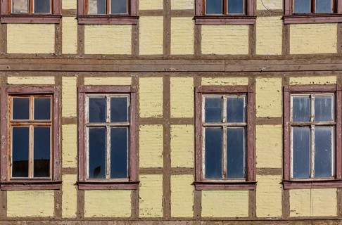 Façade of a historic half-timbered building with yellow walls and several rectangular windows with