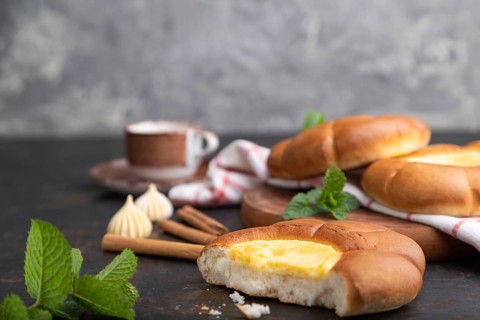 Sour cream bun with cup of coffee on a black concrete background and linen textile. Side view,