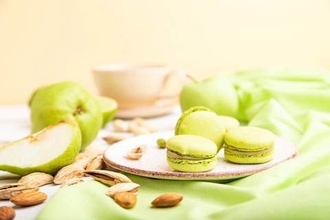 Green macarons or macaroons cakes with cup of coffee on a white wooden background and green linen