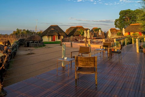 Sunset over African lodge with thatched roof huts and wooden terrace in the foreground, Namibia,