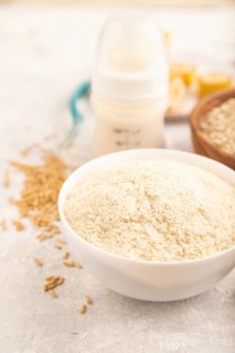 Powdered milk and oatmeal, banana baby food mix, infant formula, pacifier, bottle, spoon on gray