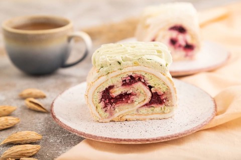 Roll biscuit cake with cream cheese and jam, cup of coffee on brown concrete background and orange