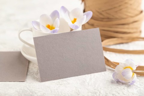 Gray paper invitation card, mockup with purple crocus snowdrop flowers on gray concrete background.