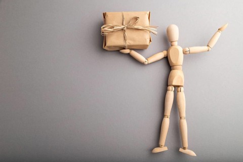 Wooden mannequin holding a gift box on gray pastel background. copy space, isolated, delivery