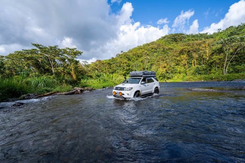 Toyota off-road vehicle with roof tent drives through a wide river in the rainforest, Alajuela