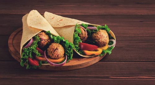 Tortillas wrapped with falafel balls and fresh vegetables, vegetarian healthy food, on a wooden