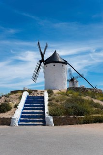 White windmill against a blue sky, flanked by a blue and white stone staircase, surrounded by