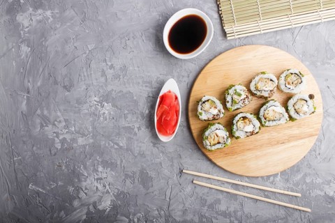 Japanese maki sushi rolls with green onion, chopsticks, soy sauce and marinated ginger on wooden