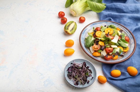 Vegetarian salad of pac choi cabbage, kiwi, tomatoes, kumquat, microgreen sprouts on a white