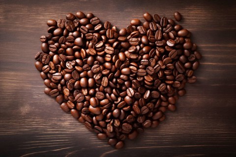 A heart shape made of rich, dark coffee beans sits atop a rustic wooden background, symbolizing a