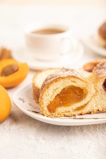 Homemade sweet bun with apricot jam and cup of coffee on gray concrete background. side view, close