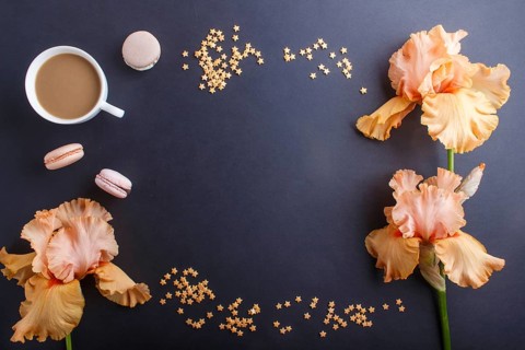 Orange iris flowers and a cup of coffee on a black background. Morninig, spring, fashion