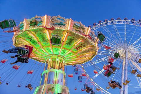 Illuminated chain carousel and Ferris wheel at night with cheerful people, funfair, wave flight,