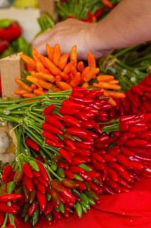 Fresh red, orange and green chilli peppers are offered at a market, accompanied by a grasping hand,