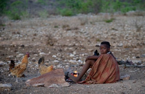 Young shepherdess from the Himba people sitting by a campfire, Ombombo, Kaokoland, Kunene, Namibia,