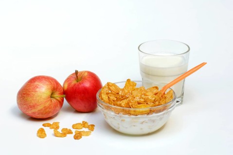 Glass bowl with cornflakes, apples, glass with milk, spoon, bowl