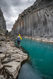 Tourist standing by the river in Stuðlagil Canyon, turquoise blue river between basalt columns,
