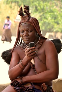 Himba woman in traditional costume typing on her mobile phone, Opuwo, Kaokoland, Kunene, Namibia,