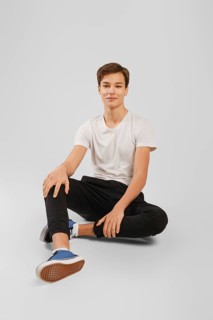 Cheerful young handsome man in black trousers and white shirt sits on the floor in studio
