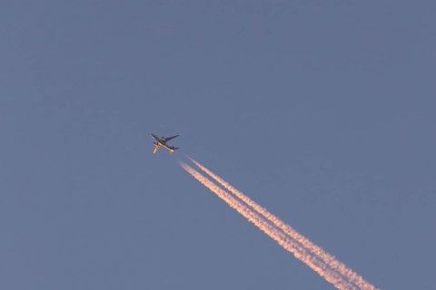 Boeing 767 jet cargo aircraft of FedEx flying in a blue sky with vapor trails or contrails behind,