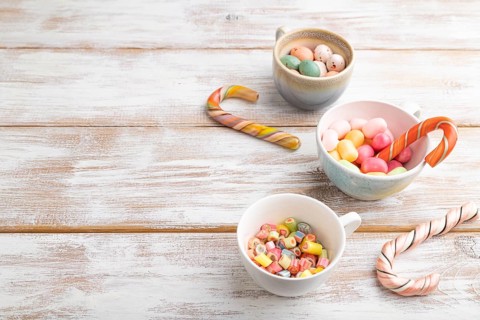 Heap of multicolored caramel candies in cups on white wooden background. copy space, side view,