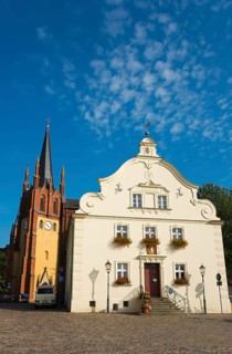 Historic church tower next to a baroque building in sunny weather with blue sky,